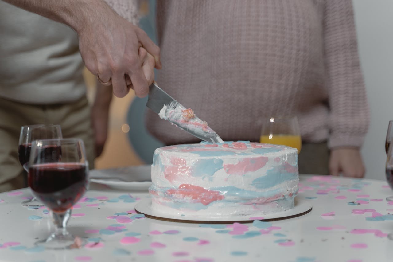 Close-up of a gender reveal cake being sliced with hands visible, surrounded by drinks.