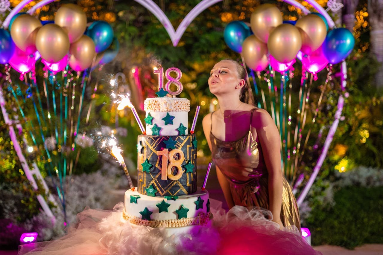 A young woman celebrates her 18th birthday with a colorful cake surrounded by balloons and sparklers.